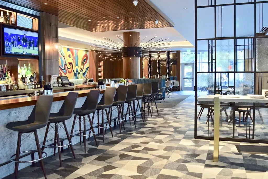Modern bar with a long counter, stools, and sports on TV.