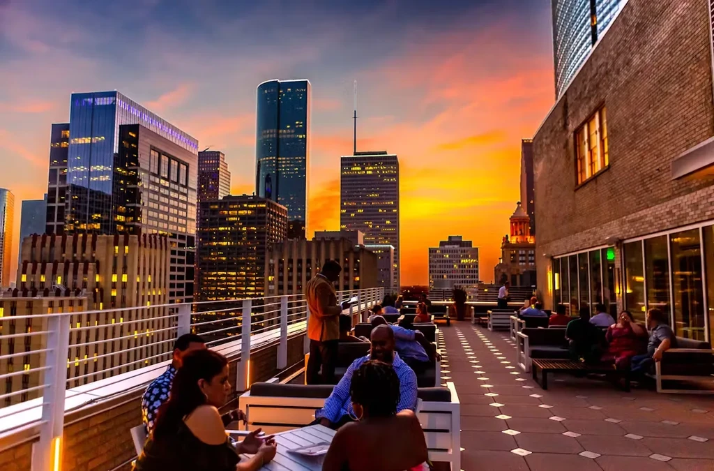 Rooftop bar at dusk overlooking city skyline with people.