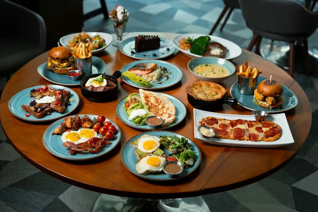 Round wooden table laden with diverse dishes like French toast, burgers, and salmon.