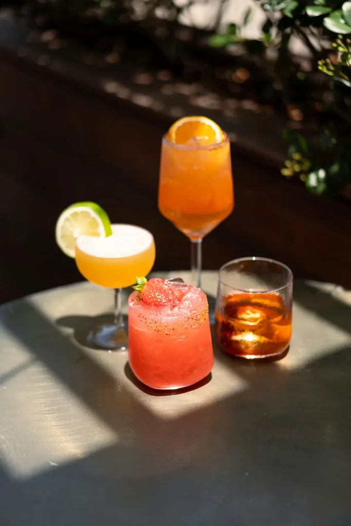 Four cocktails with garnishes on a round outdoor table.