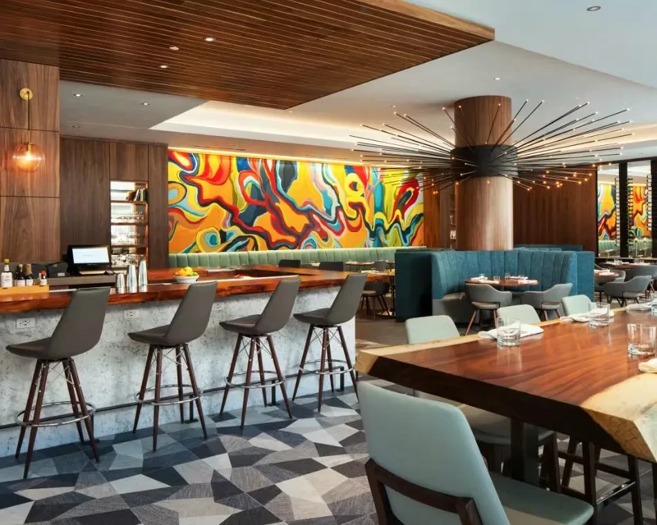 Modern restaurant interior with a wooden bar, tables, and a colorful mural.