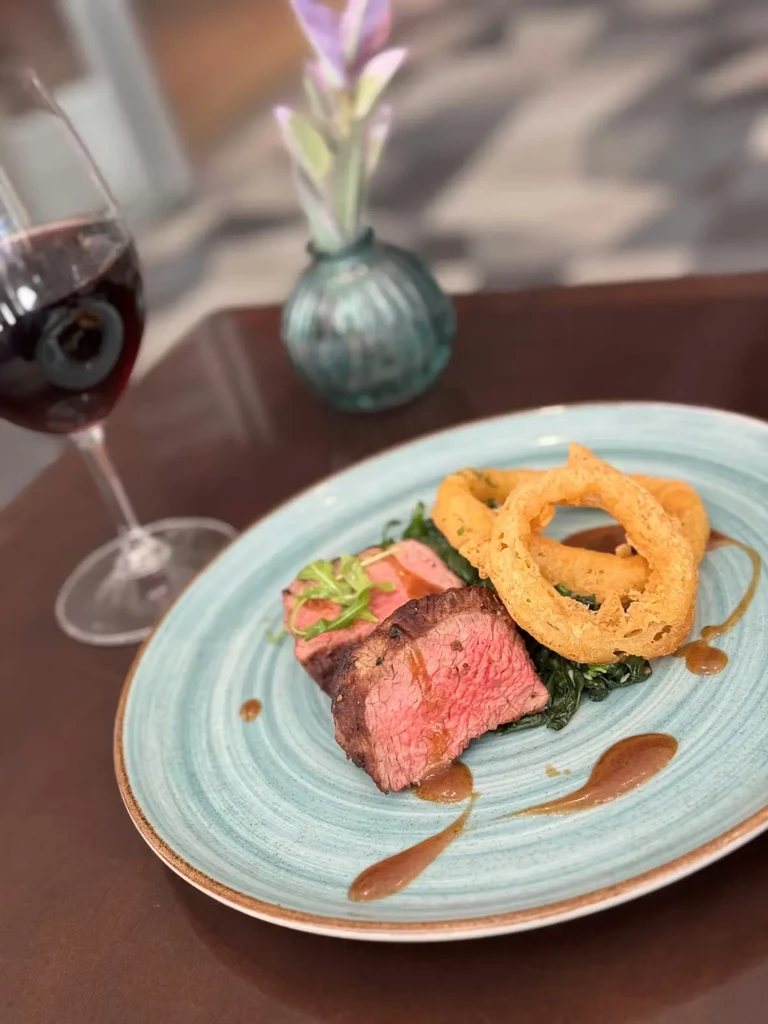 Two medium-rare steaks with onion rings, vegetables, and red wine.