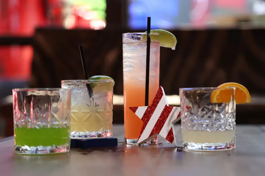 Four cocktails: one green, one yellow, one orange-pink, one clear.