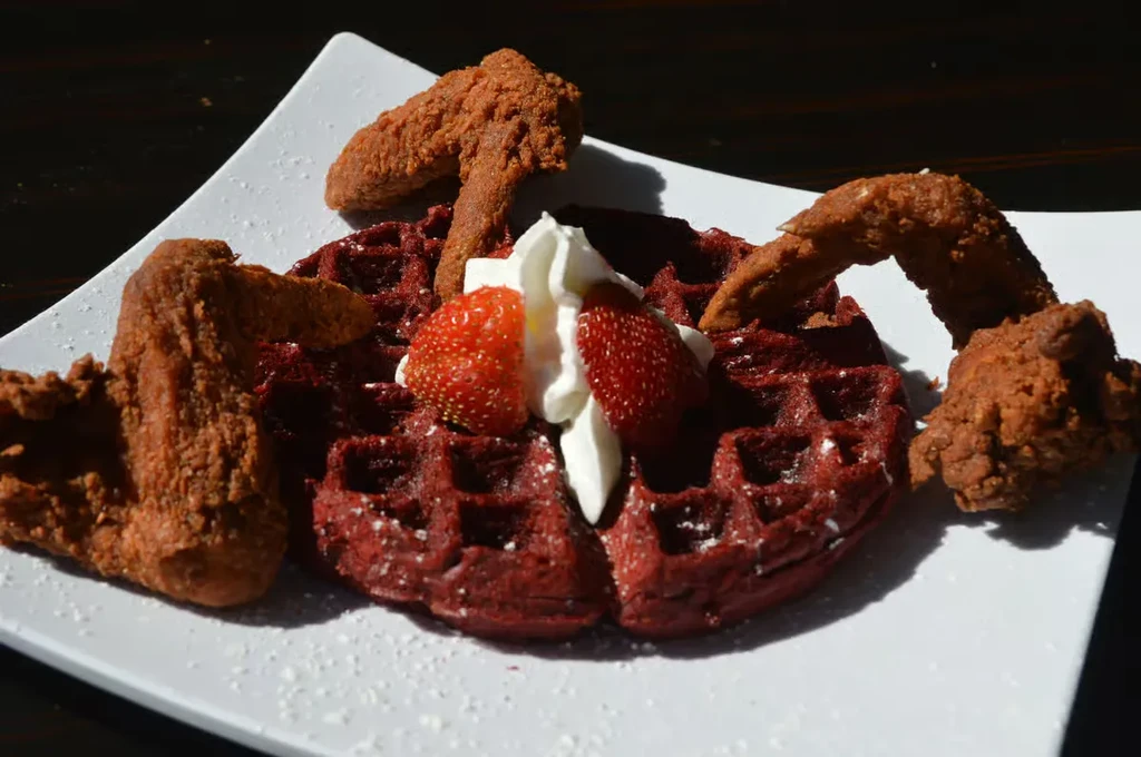 Red velvet waffle with fried chicken, strawberries, and whipped cream.