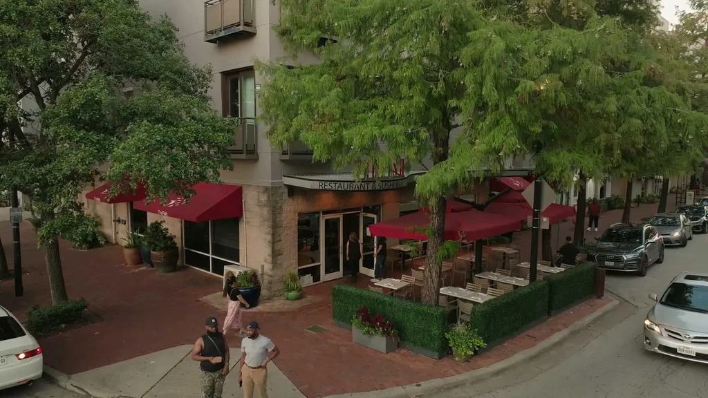 Aerial shot of a restaurant with red awnings, outdoor seating, and trees.