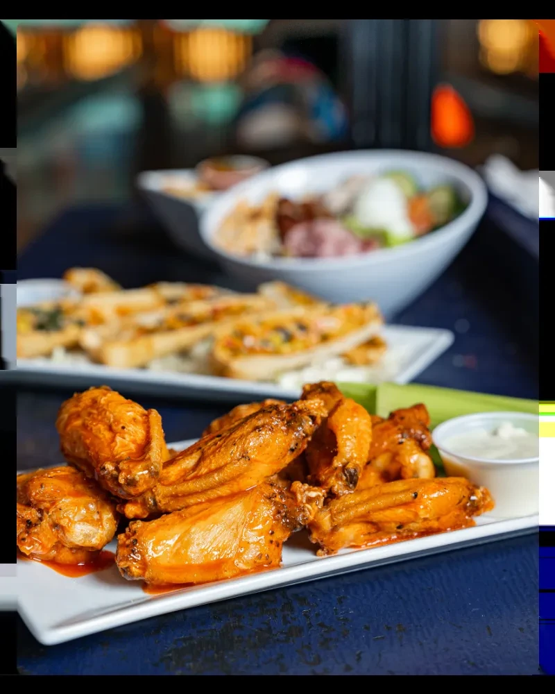 Close-up of chicken wings, toasts, and salad on a dark blue table.