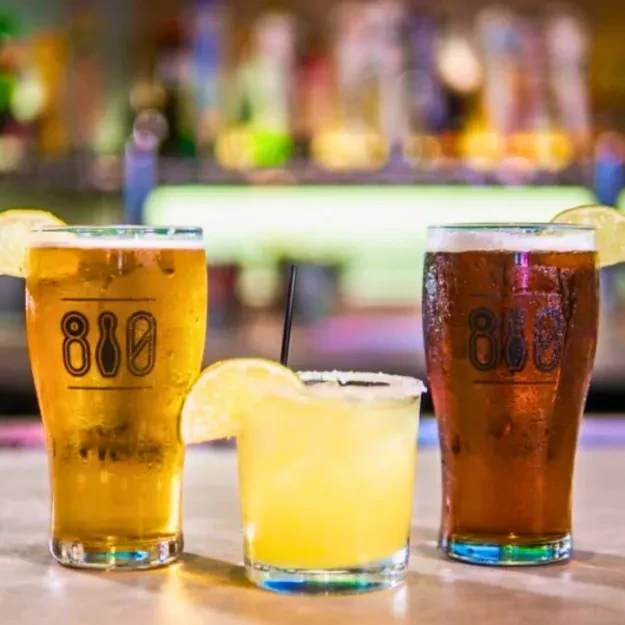 Three drinks on a bar: two beers, one cocktail, all with lime.