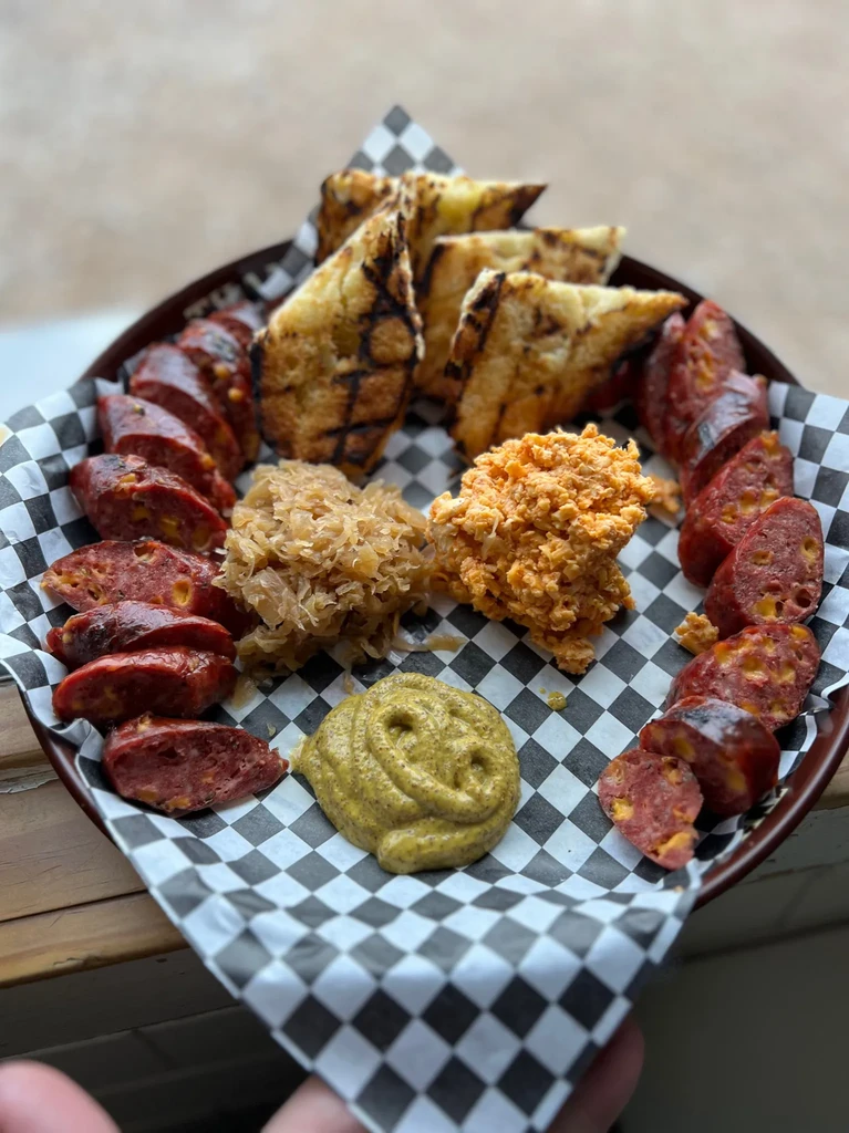 Appetizer platter with sausage, toast, sauerkraut, pimento cheese, and mustard.