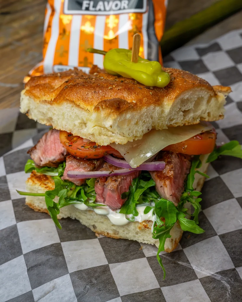 Gourmet steak sandwich on focaccia with arugula, tomato, and onion.