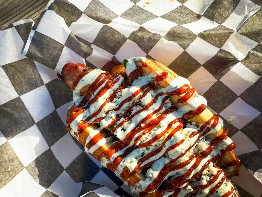 Hot dog in bun with two sauces and crumbled cheese.