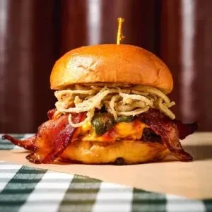 Close-up of a burger with bacon, jalapeños, and fried onion strings.