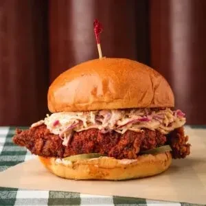 Fried chicken sandwich with coleslaw, pickles, and a red toothpick.