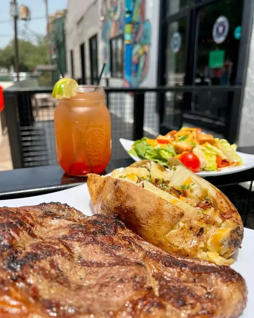 Grilled steak, loaded baked potato, salad, and a drink.