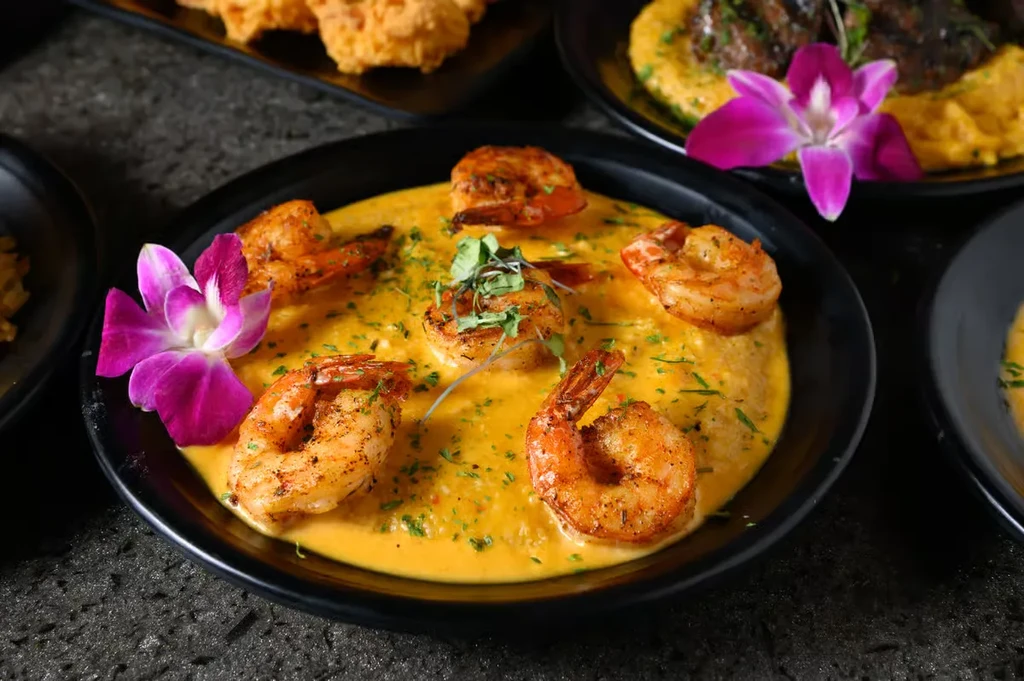 Shrimp and grits in a dark bowl, garnished with herbs.