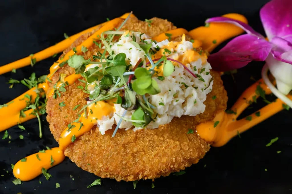 Golden-brown crab cake topped with crab meat, greens, and orange sauce.