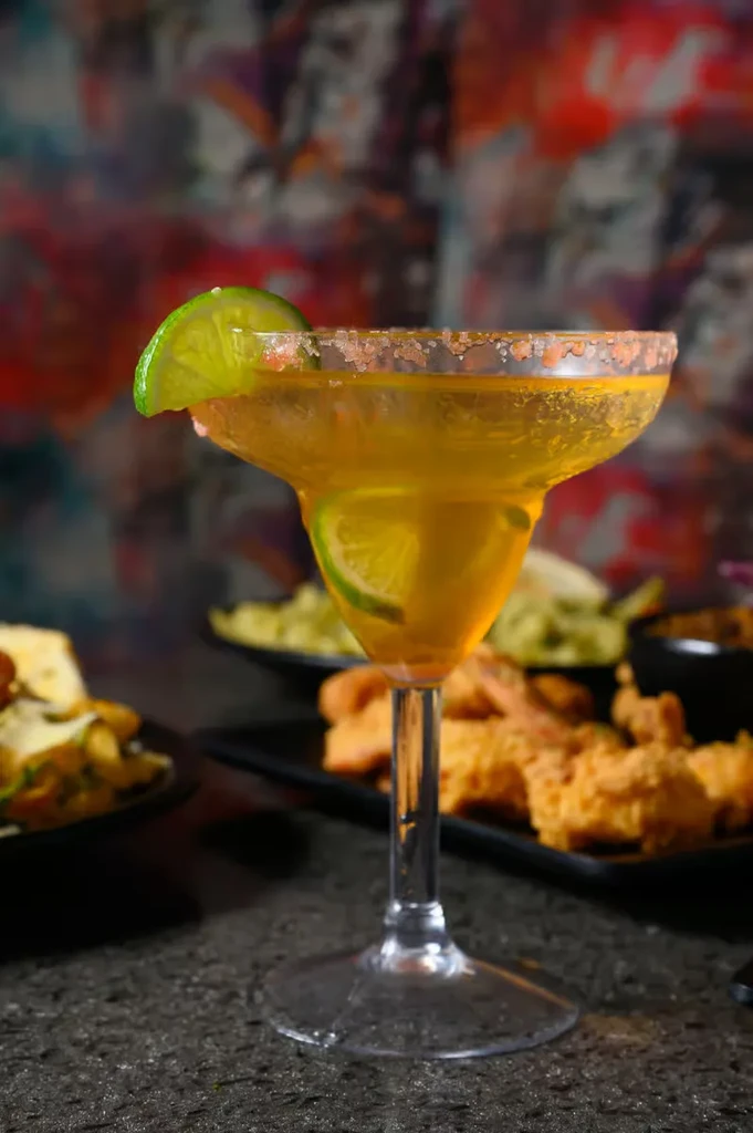 Yellow cocktail with lime wedge and salted rim.