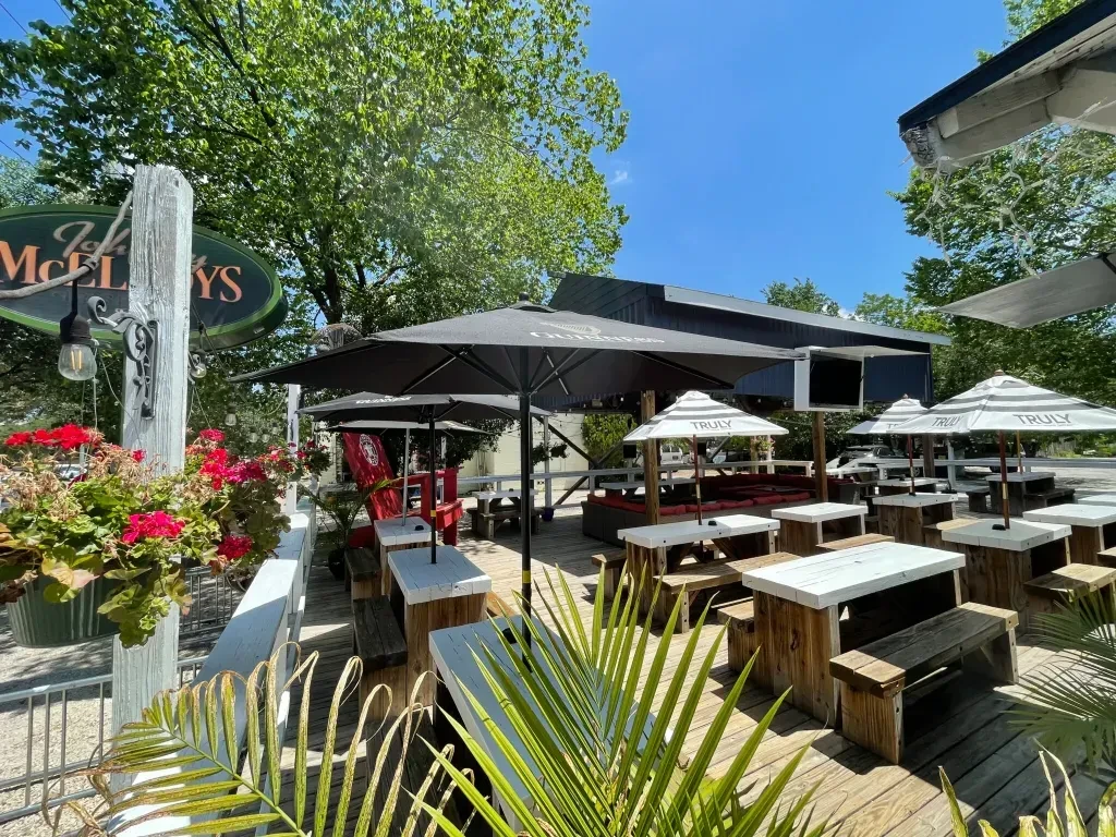 Sunny restaurant patio with picnic tables, lounge seating, and umbrellas.