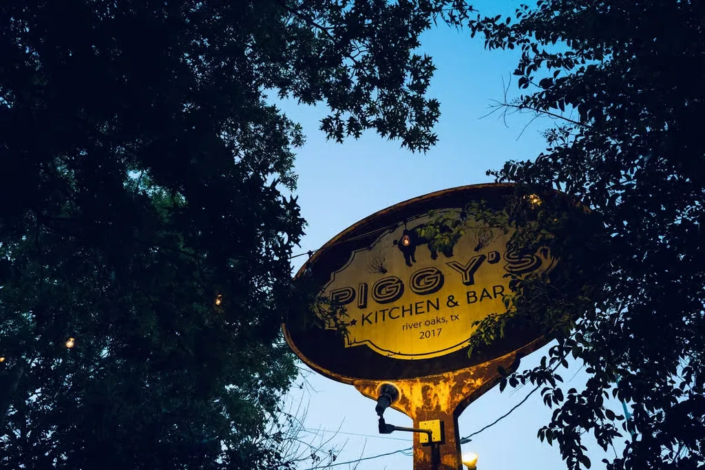 Outdoor metal sign for Piggy's Kitchen & Bar, lit from below.