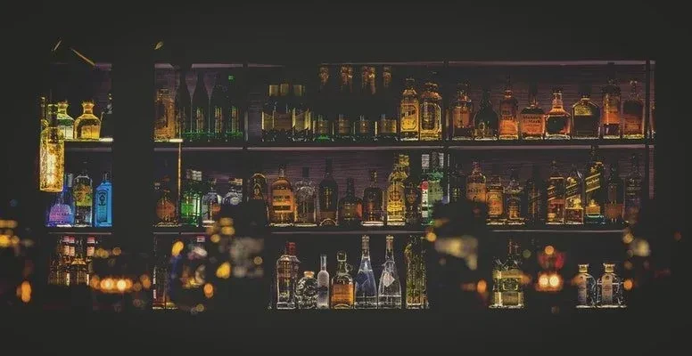 Well-stocked bar shelves with various bottles of alcohol and atmospheric lighting.