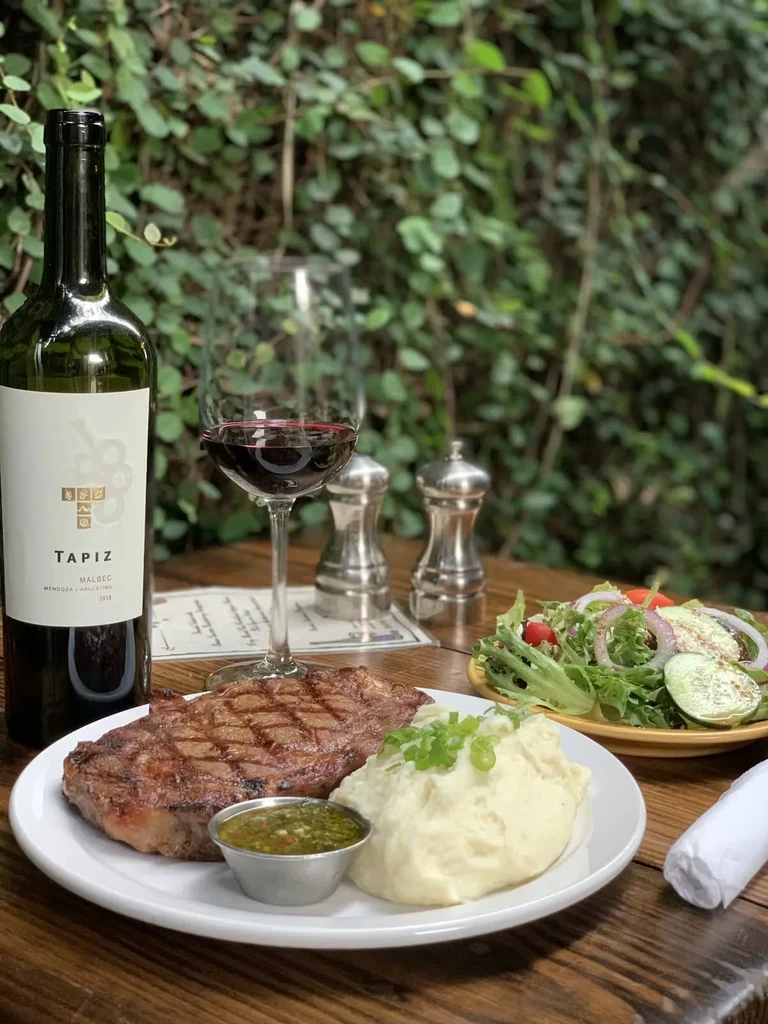 Grilled steak, mashed potatoes, salad, and red wine on an outdoor table.