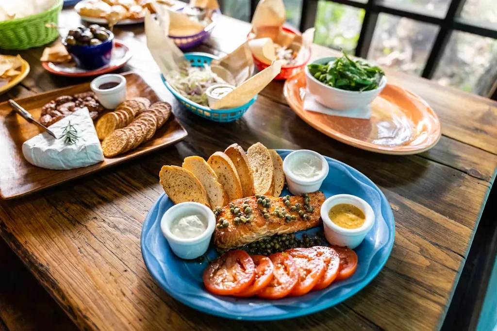 Grilled salmon with capers, tomatoes, bread, and various side dishes.