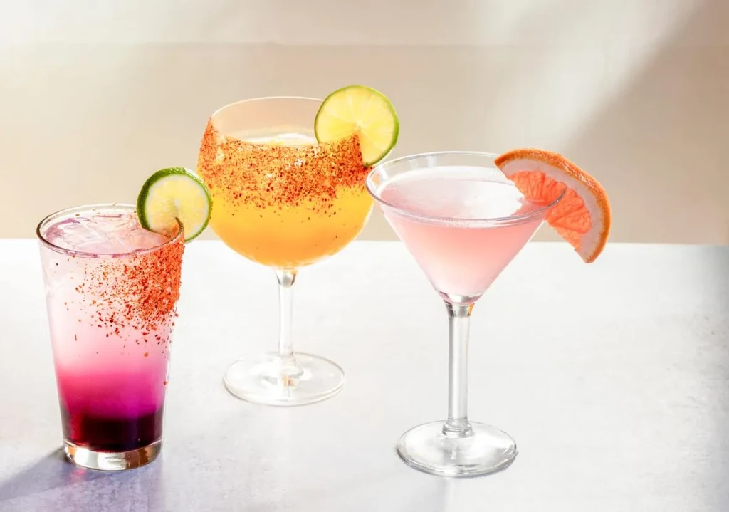 Three cocktails with lime and grapefruit garnishes on a light surface.