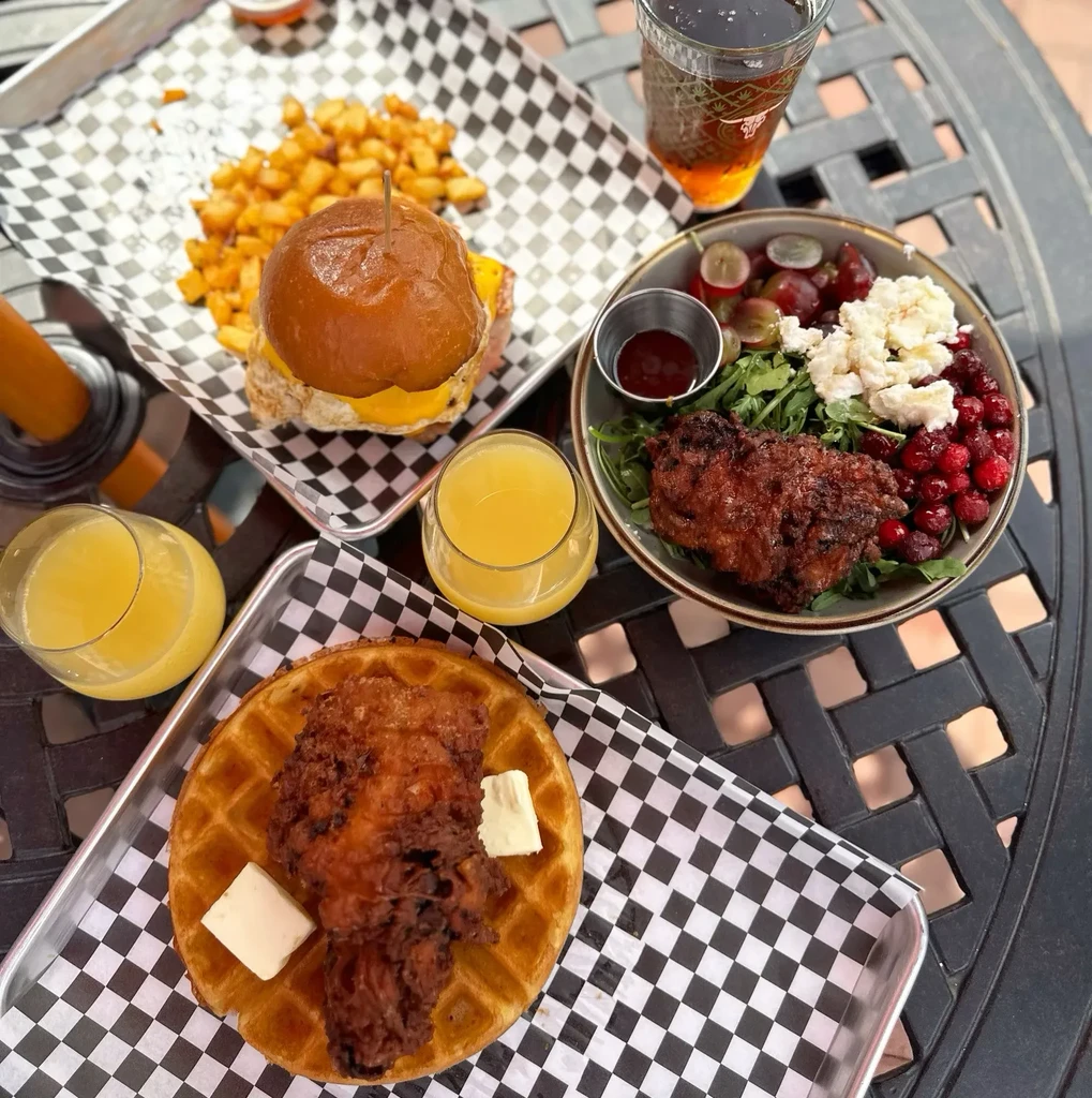 Breakfast or brunch spread with burger, waffle, salad, and drinks.