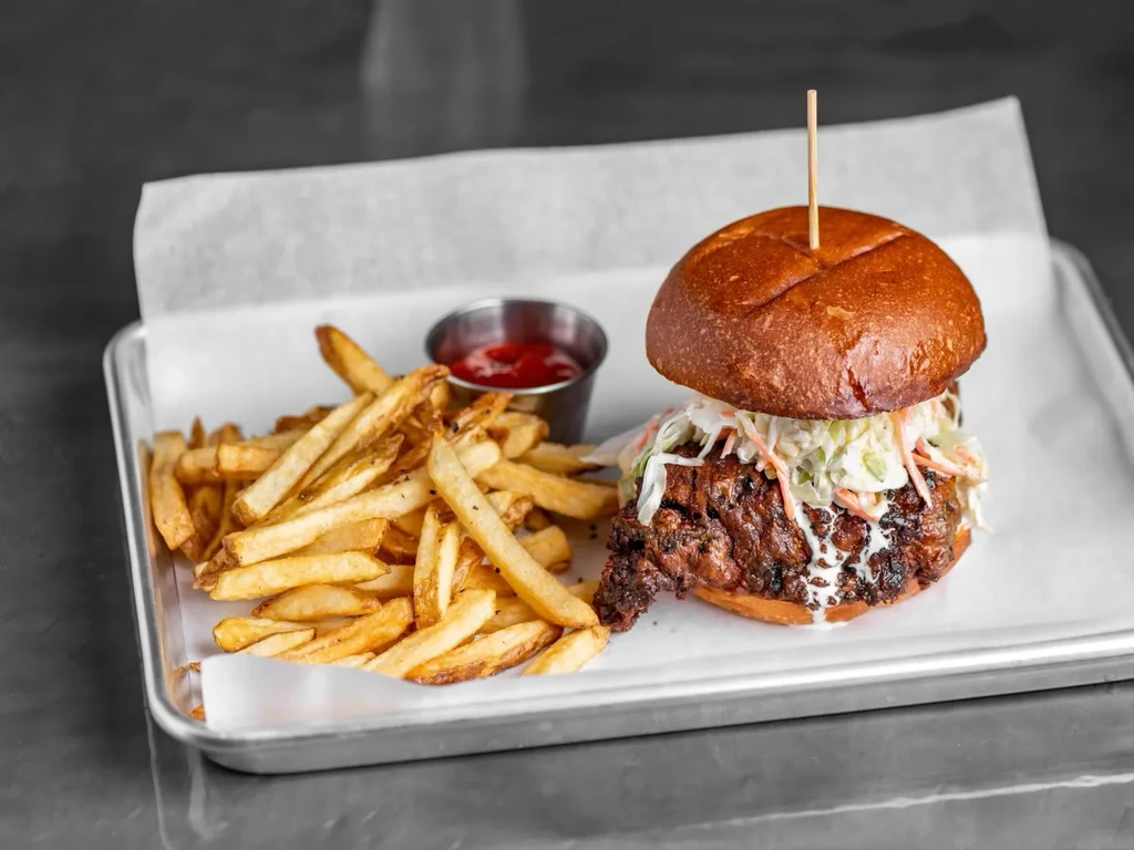 Fried chicken sandwich, coleslaw, french fries, and ketchup on metal tray.