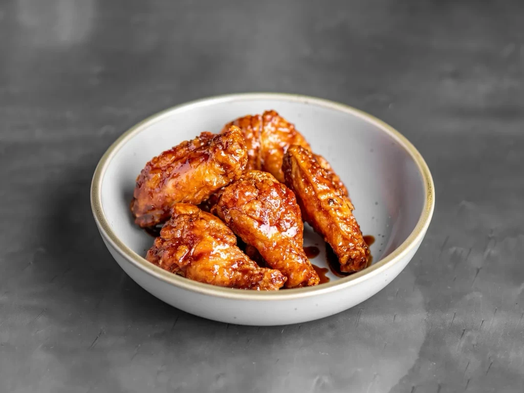 Ceramic bowl of five dark orange glazed chicken wings.