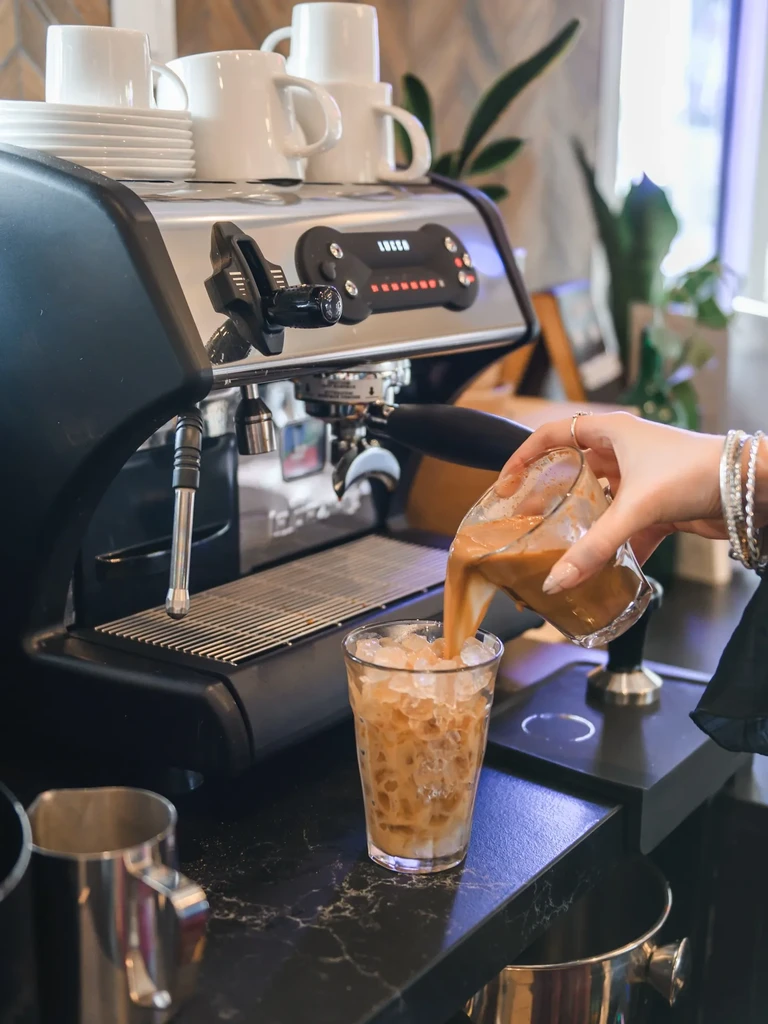 Hand pours coffee into a glass of ice and milk.