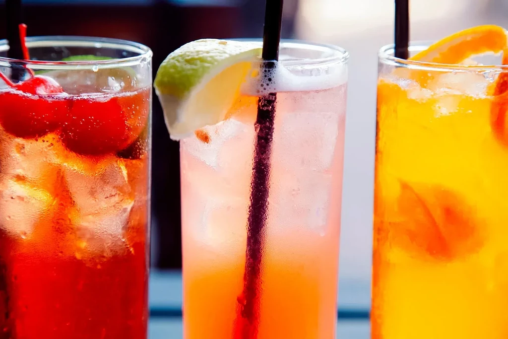 Three vibrant, cold drinks in clear glasses with garnishes.