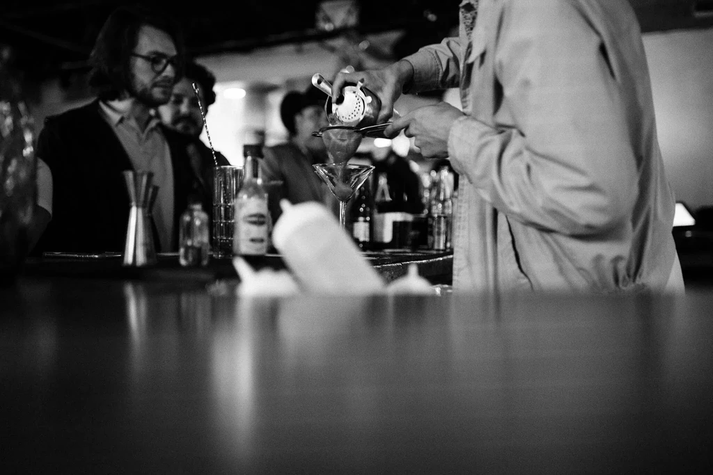 Bartender pours a drink for patrons at a dimly lit bar.