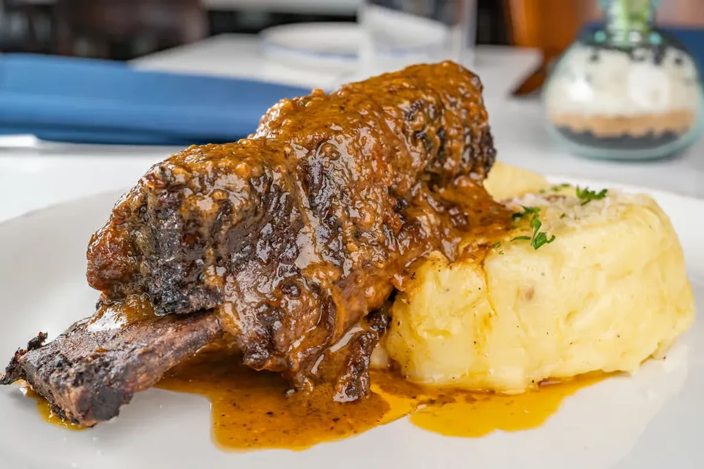 Braised short rib on a white plate with mashed potatoes.