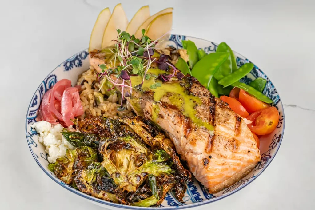 Grilled salmon with vegetables, brown rice, and pear in a white bowl.