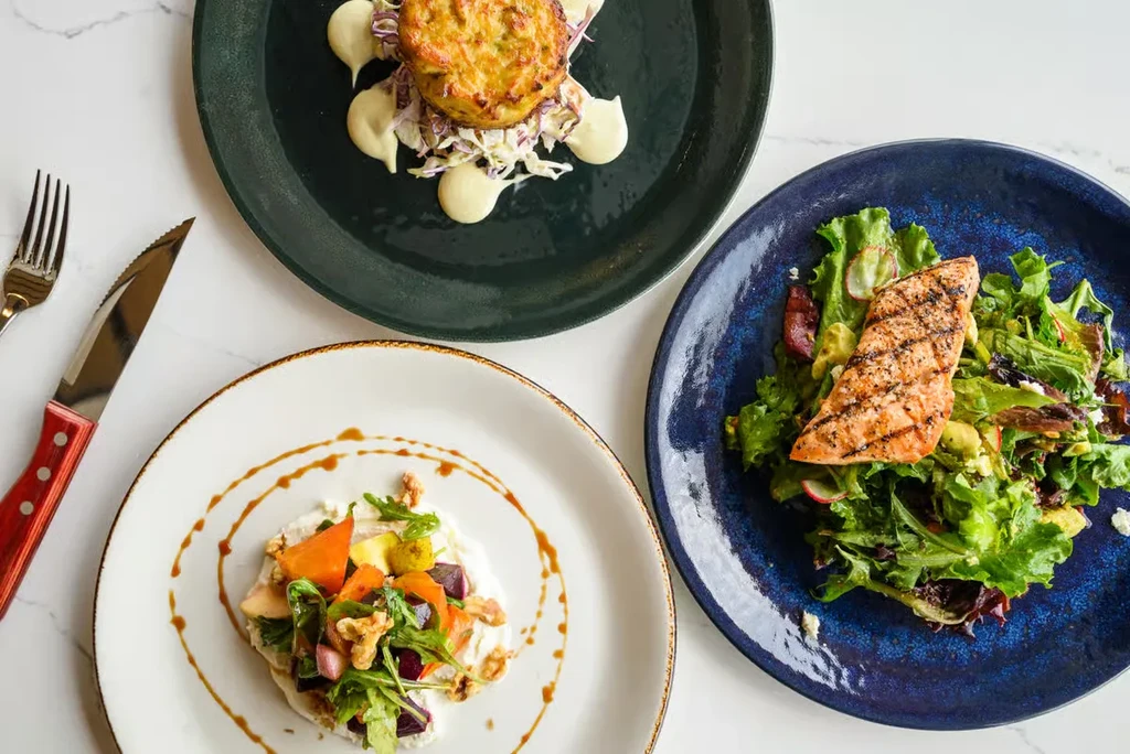 Three plates of food: fritter, salmon, and salad on a table.