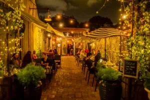 Outdoor patio at night with string lights, diners, and potted plants.