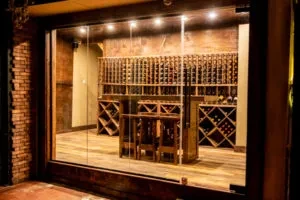 A wine cellar seen through glass, filled with bottles and a table.