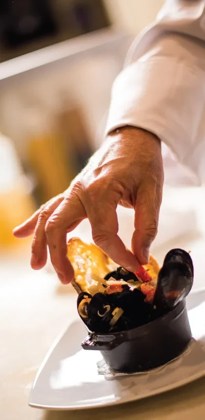 Chef garnishing a bowl of mussels with red ingredients.