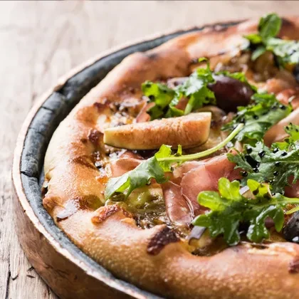 Gourmet pizza with prosciutto, arugula, figs, and olives in a metal pan.