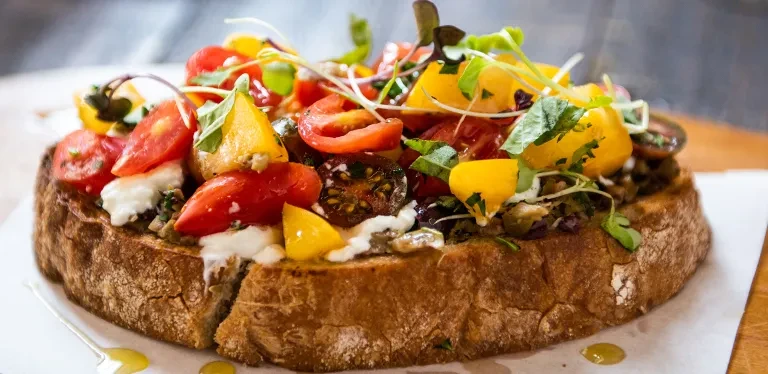 Rustic bread topped with tomatoes, cheese, herbs, and sprouts.
