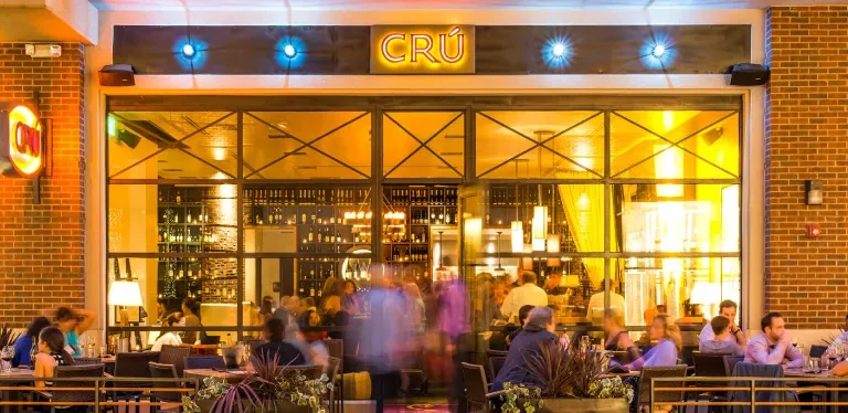 Exterior of CRÚ restaurant with outdoor patio and patrons at night.