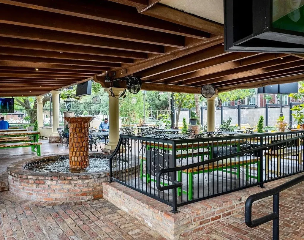 Outdoor restaurant patio with brick fountain, picnic tables, and trees.
