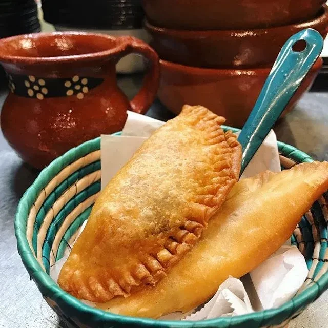 Fried pastries in a woven basket with ceramic mug and bowls.