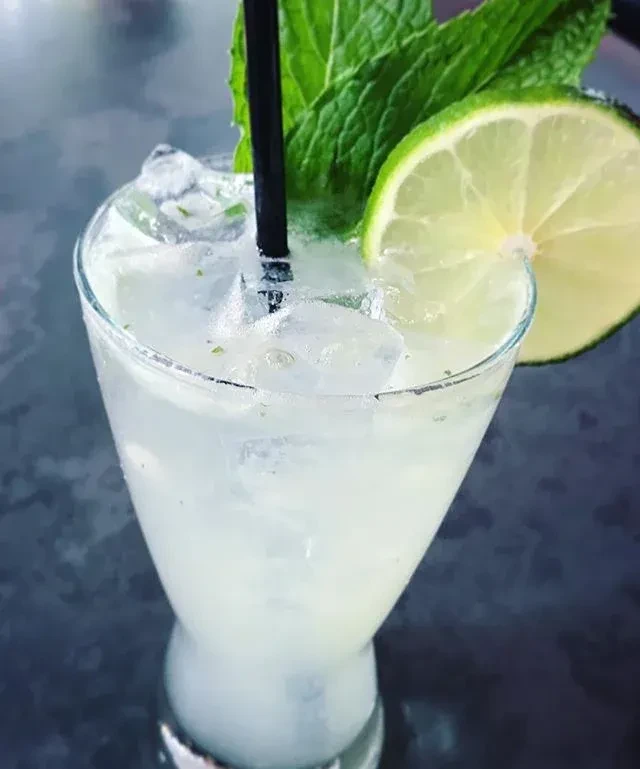 Lime cocktail in a tall glass, garnished with mint.