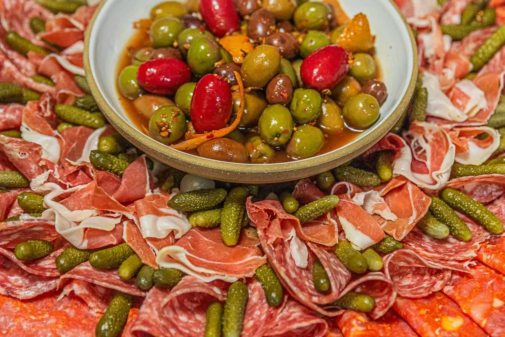 Close-up of a charcuterie board with olives, cured meats, and gherkins.