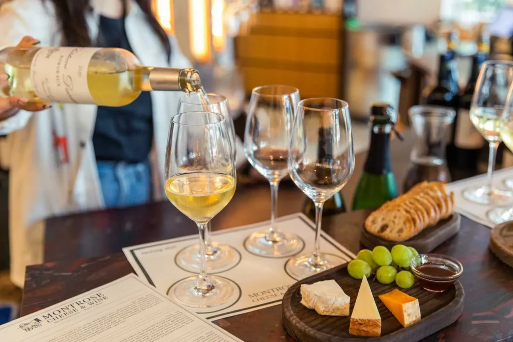 Hand pouring white wine into a glass at a tasting event.