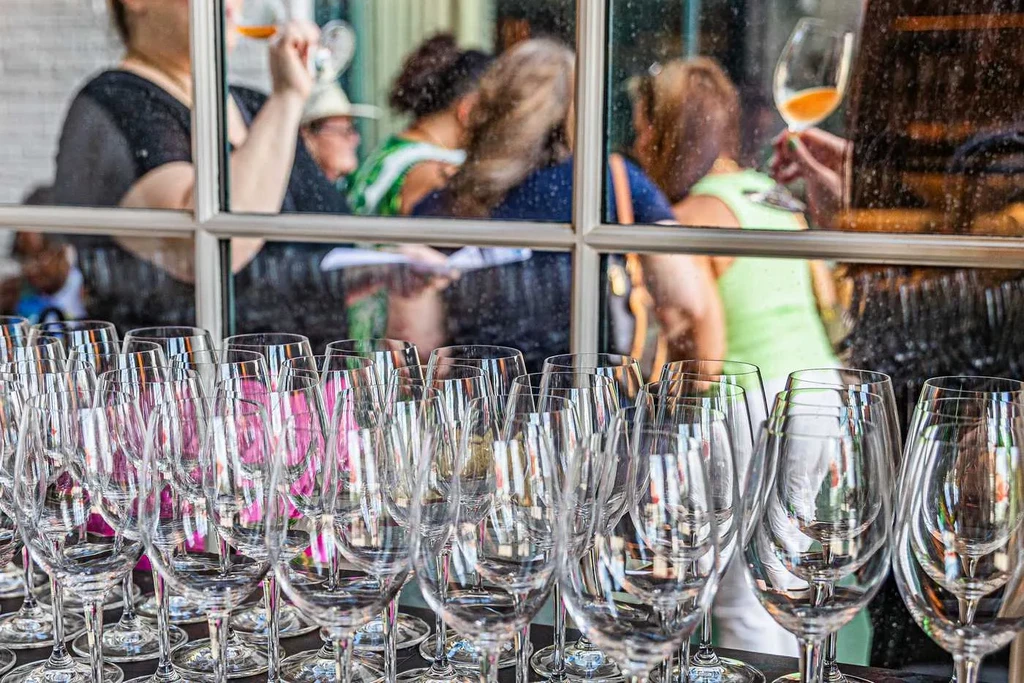 Empty wine glasses in rows, people with drinks in the background.