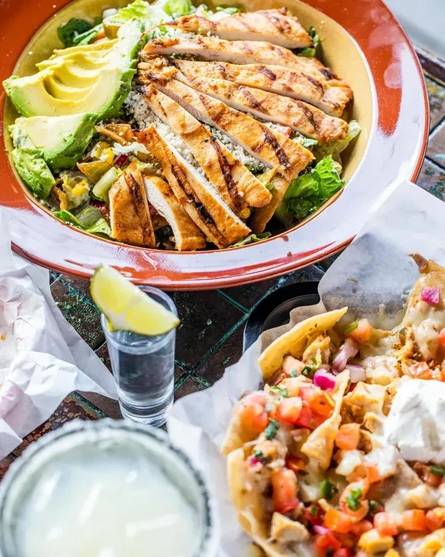 Overhead shot of a colorful salad, nachos, and drinks on a table.