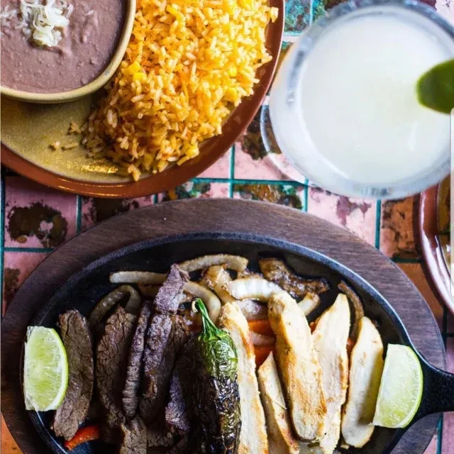 Overhead shot of fajitas, rice, beans, and a drink on a table.