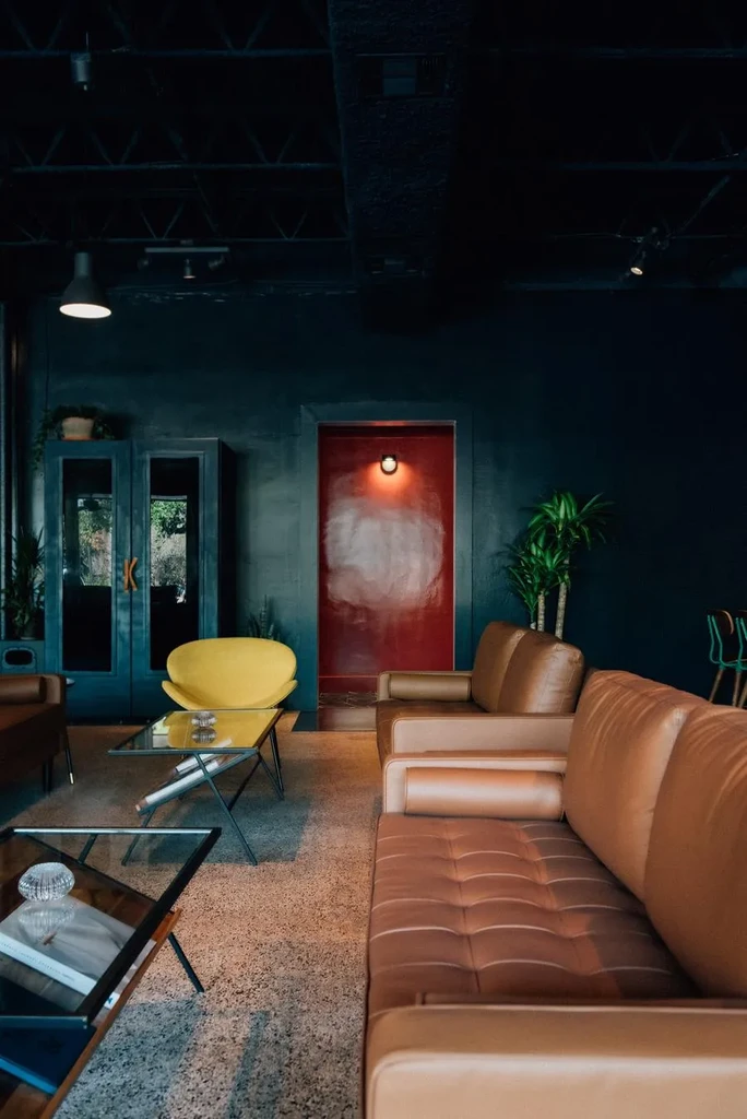 Modern lounge with yellow chair, two tan sofas, and red doorway.
